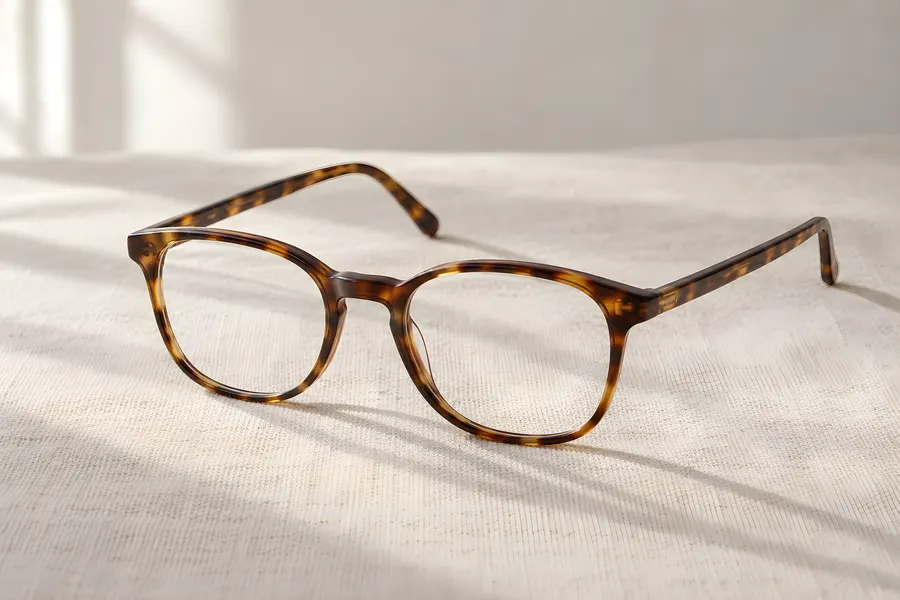 Eine offene Brille mit Fassung in Schildpattoptik steht auf hellem Leinen, weiches Fensterlicht